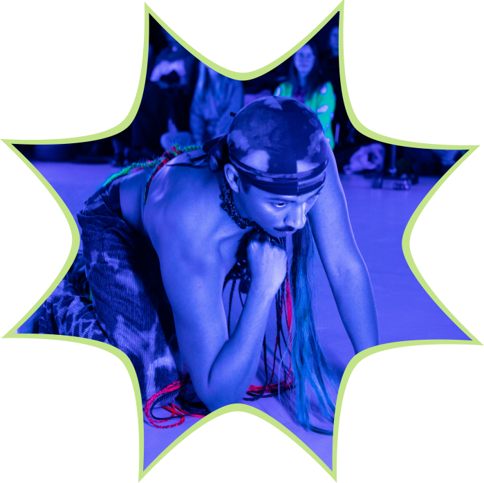 A person resting their head on ther knuckle wearing a durag in a blue lit room.