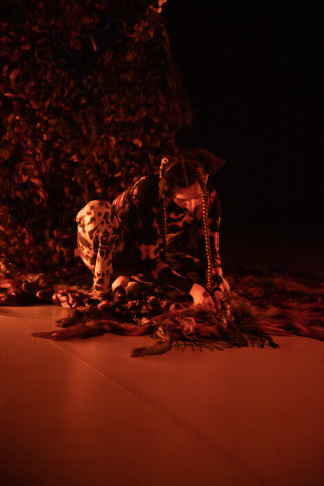 A person braiding their hair into a long weave in a warmly lit room with an orange tint.