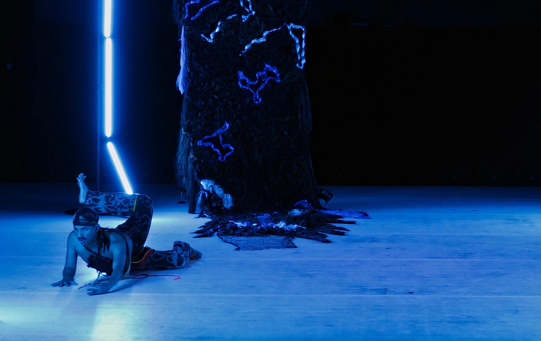 A person lying on their stomach in a blue lit room with their leg up in the air like if it was a fin.